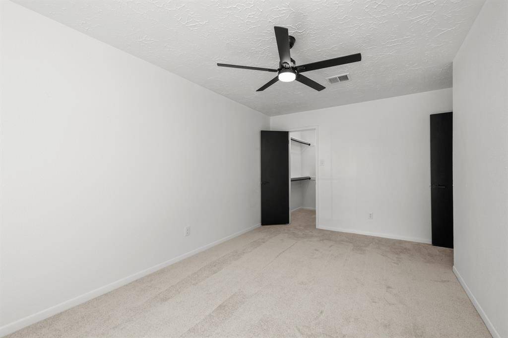 This spacious living room features a high vaulted ceiling with a central beam, warm wood like flooring, and a striking brick fireplace. Large windows provide ample natural light, creating an inviting atmosphere.