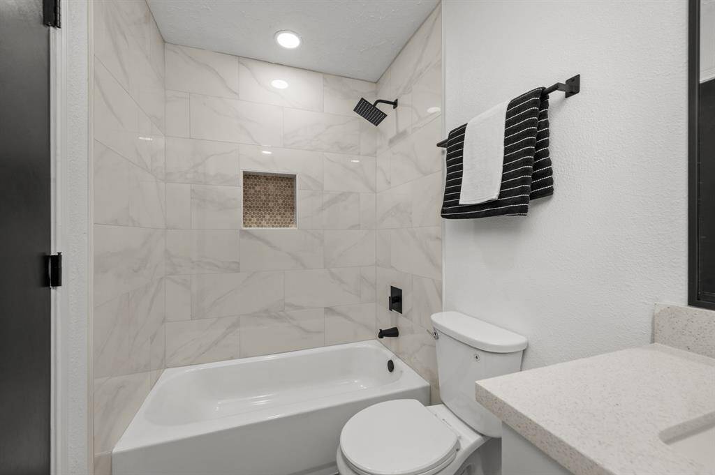 This guest bathroom features a modern design with a sleek white bathtub and marble-style tile surround. It includes a built-in shower niche, black fixtures, and a matching towel set, creating a clean and contemporary look.