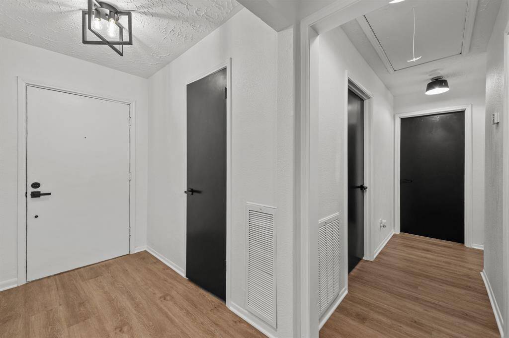 The entrance of the home shows a modern hallway featuring light wood like LVT flooring and bright white new painted walls throughout the home with sleek black doors. The space is well-lit with contemporary new light fixtures, offering a clean and minimalist look.
