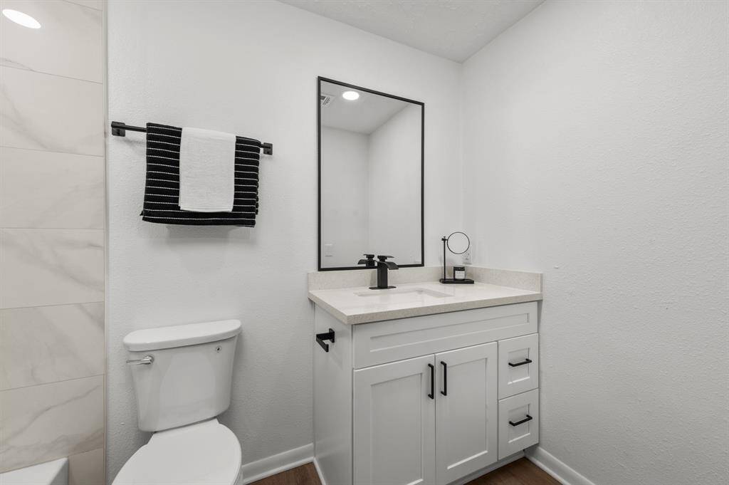 This primary bathroom features a modern design with a sleek white vanity, black hardware, and a large custom mirror. It includes a brand new toilet and new fixtures, set against a clean, white backdrop for a fresh and inviting look.