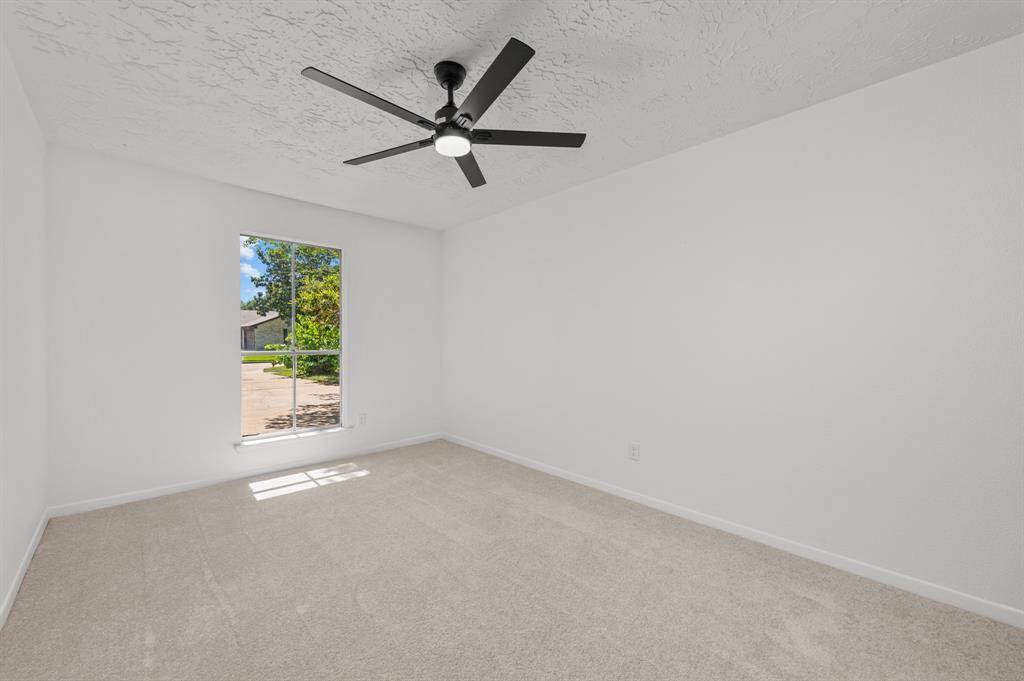 Bright, bedroom room with a large window, facing the front of the home with neutral new carpet, and a modern ceiling fan. Ideal for customization.