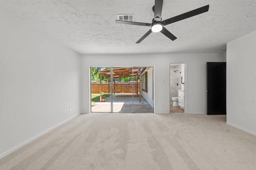Bright and spacious primary bedroom with neutral new carpeting, featuring a new modern ceiling fan and large sliding glass doors that opens to a covered patio. The room also includes an ensuite bathroom with modern fixtures. This bedroom provides tons of light into the room.