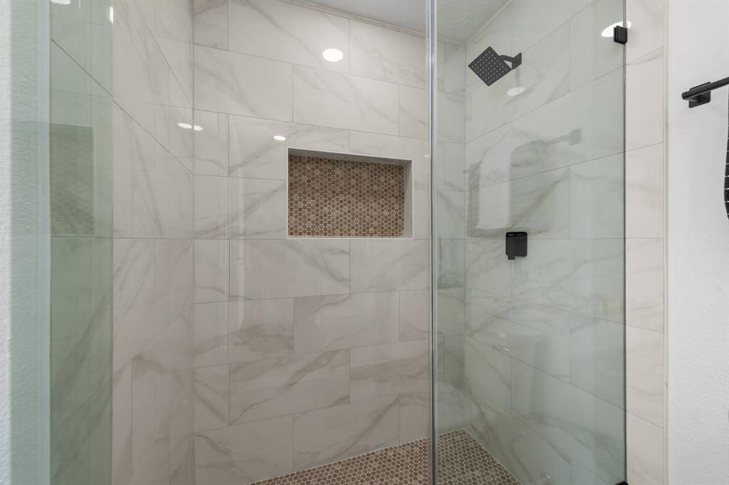 This is a modern shower with elegant marble-patterned tiles, a sleek black showerhead, and a built-in niche for storage. The glass enclosure adds a spacious and contemporary feel.
