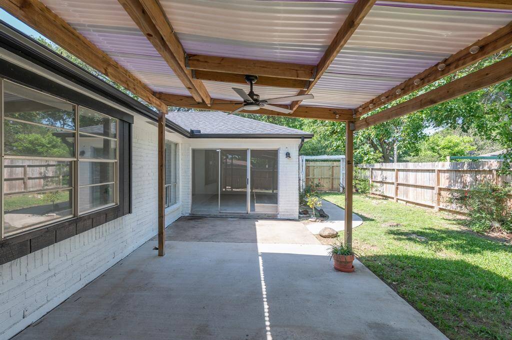 This covered patio area with two ceiling fans, perfect for outdoor relaxation. It leads to a fenced backyard, offering privacy and greenery, and features sliding glass doors that open into the house.