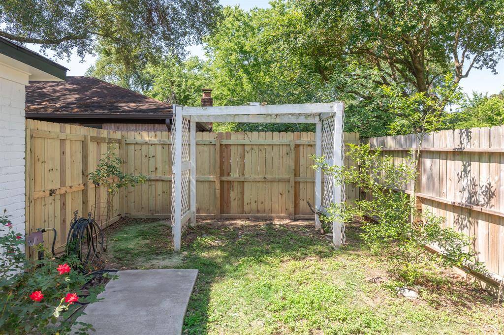 A cozy backyard space with a wooden fence and a small arbor, perfect for gardening or relaxing. It features some greenery and a concrete path leading from the house.