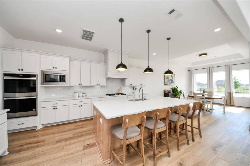 This modern kitchen features white cabinetry, stainless steel appliances, and a large island with seating. The open layout flows into a bright dining area with large windows, offering plenty of natural light and scenic views.