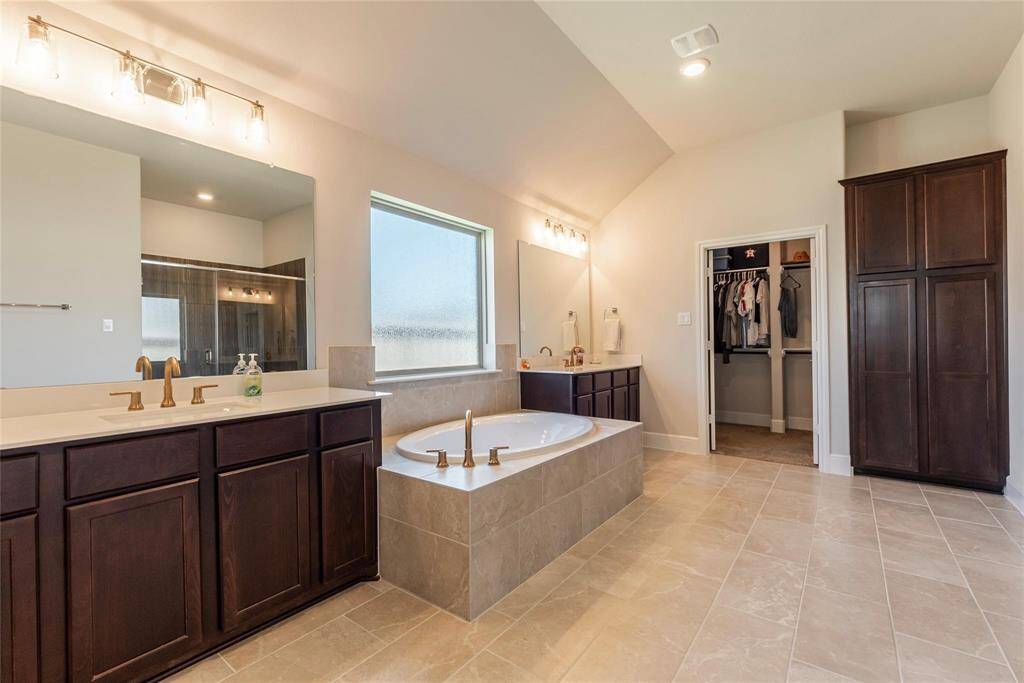 Spacious primary bath with high ceilings, tile flooring, dual vanities and separate tub.