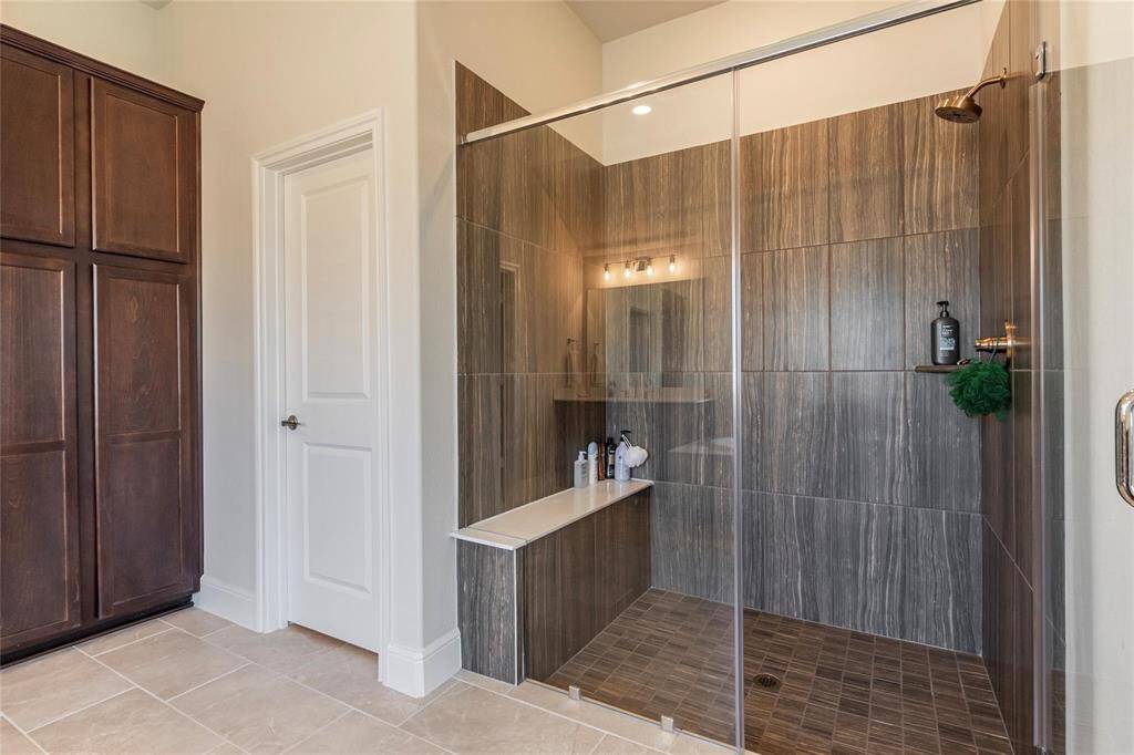 Updated walk-in shower with tile surrounding, bench and glass doors.