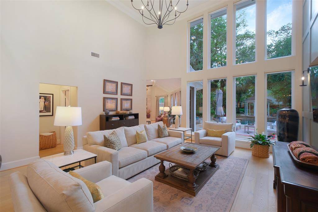 This Living Room scene features a soaring ceiling and panoramic windows with custom Hunter Douglas remote shades and an elegant chandelier. Recently professionally installed Hardwoods, Wide-Plank White Oak Flooring, throughout the residence, except in the Kitchen, Baths, and Laundry room.