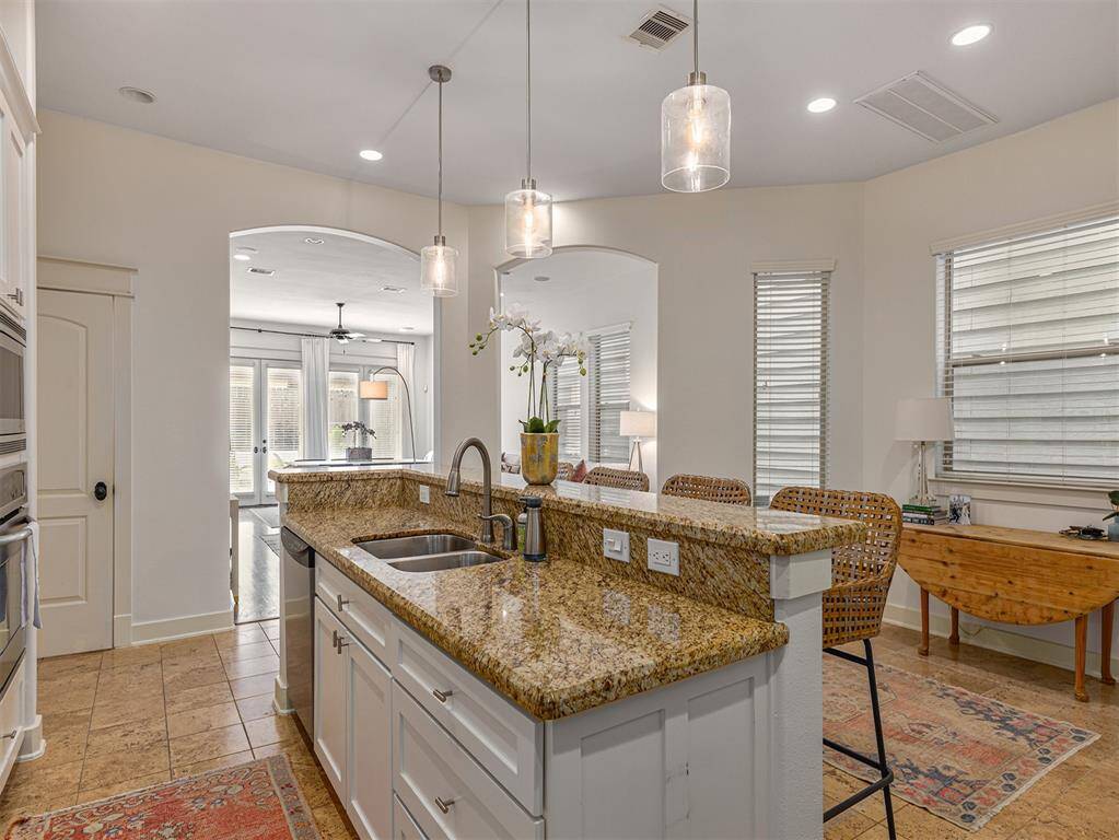 This modern kitchen features granite countertops, an island with a sink, and elegant pendant lighting. It has an open layout leading to a bright living area with large windows and stylish furnishings, creating a welcoming space for entertaining.