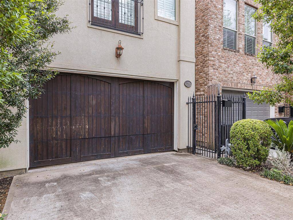This photo showcases a charming home exterior featuring a rustic wooden garage door, a gated entry, and a well-maintained driveway. The property is complemented by lush greenery and a brick facade, offering both style and security.
