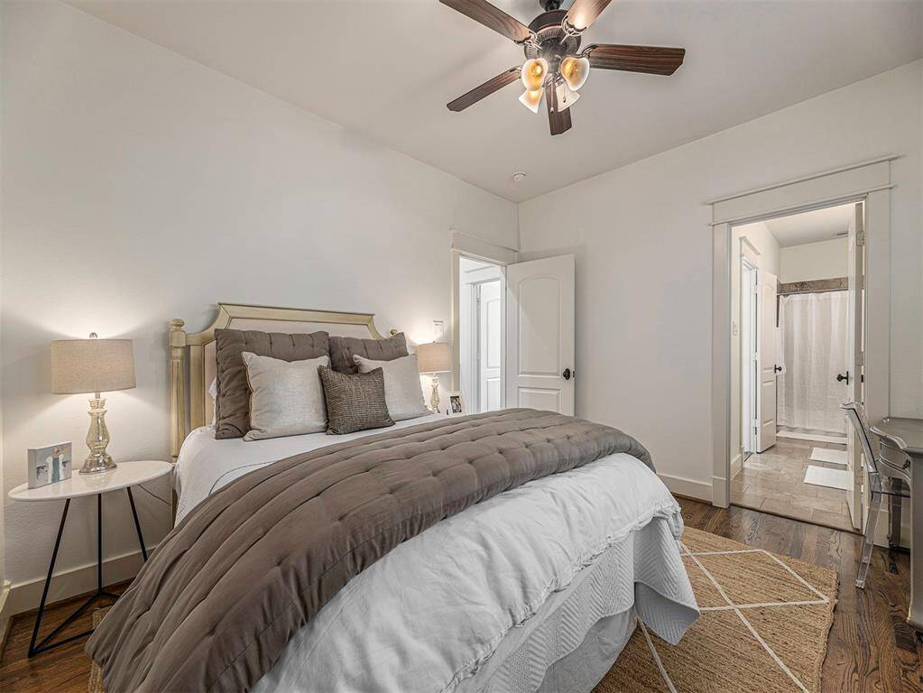 Cozy bedroom with a neutral color palette, featuring a comfortable bed, stylish ceiling fan, and hardwood floors. The room offers access to an en-suite bathroom through an open doorway, providing convenience and privacy.