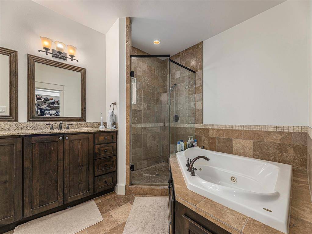 This bathroom features a stylish design with a glass-enclosed shower, a luxurious soaking tub, and a dual-sink vanity with granite countertops and dark wood cabinets, creating a warm and inviting space.