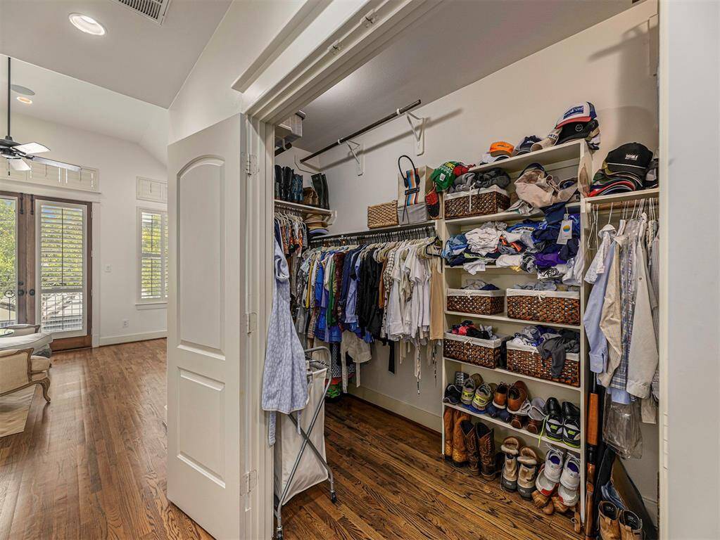 This photo shows a spacious walk-in closet with ample shelving and hanging space, adjacent to a bright room with hardwood floors and French doors leading outside, creating an elegant and functional storage area.