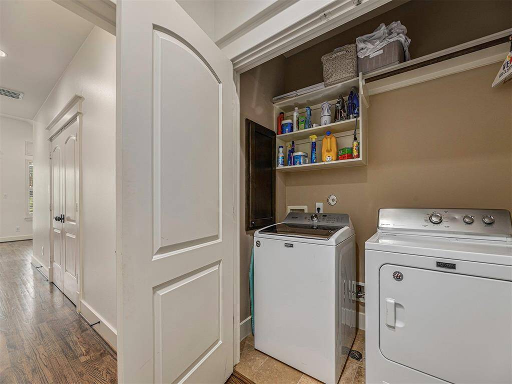 This is a compact laundry area with a washer and dryer, built-in shelving for storage, and a folding door. It's located off a hallway with hardwood floors, offering convenience and functionality.
