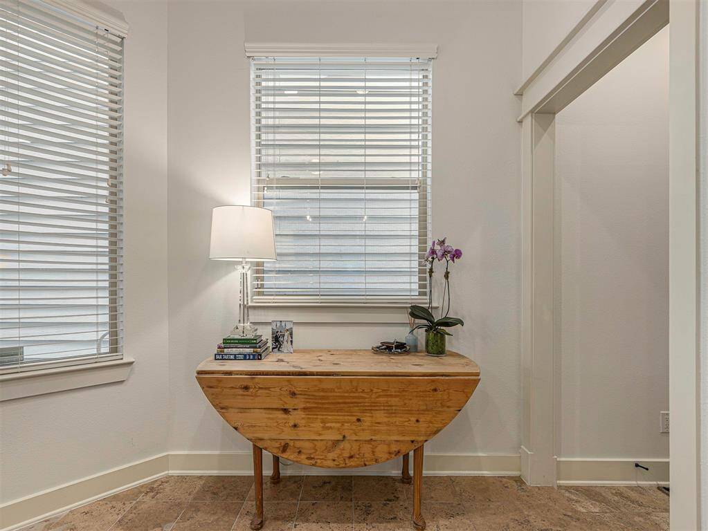 This cozy nook features a wooden drop-leaf table with a lamp, books, and an orchid, set against bright windows with blinds. The space is perfect for a reading or work area.