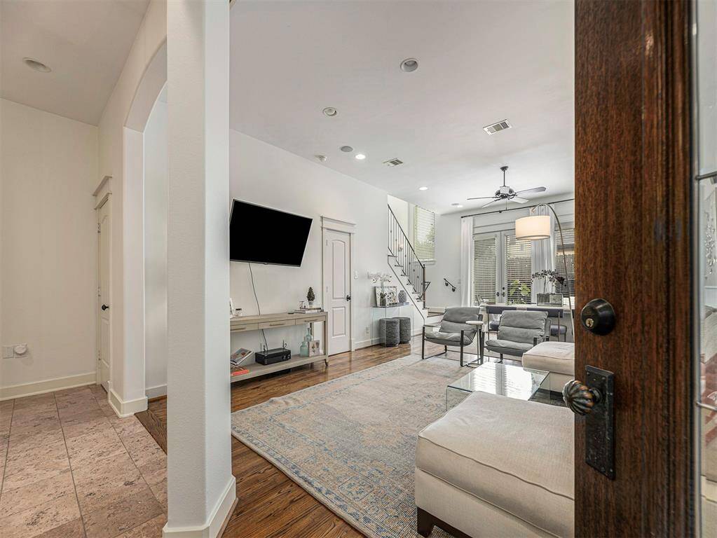 This photo showcases a modern, open living space with hardwood floors, neutral walls, and ample natural light. The room features a cozy seating area, a wall-mounted TV, and a dining space beneath a stylish light fixture. A staircase leads to the upper level, adding an elegant touch.