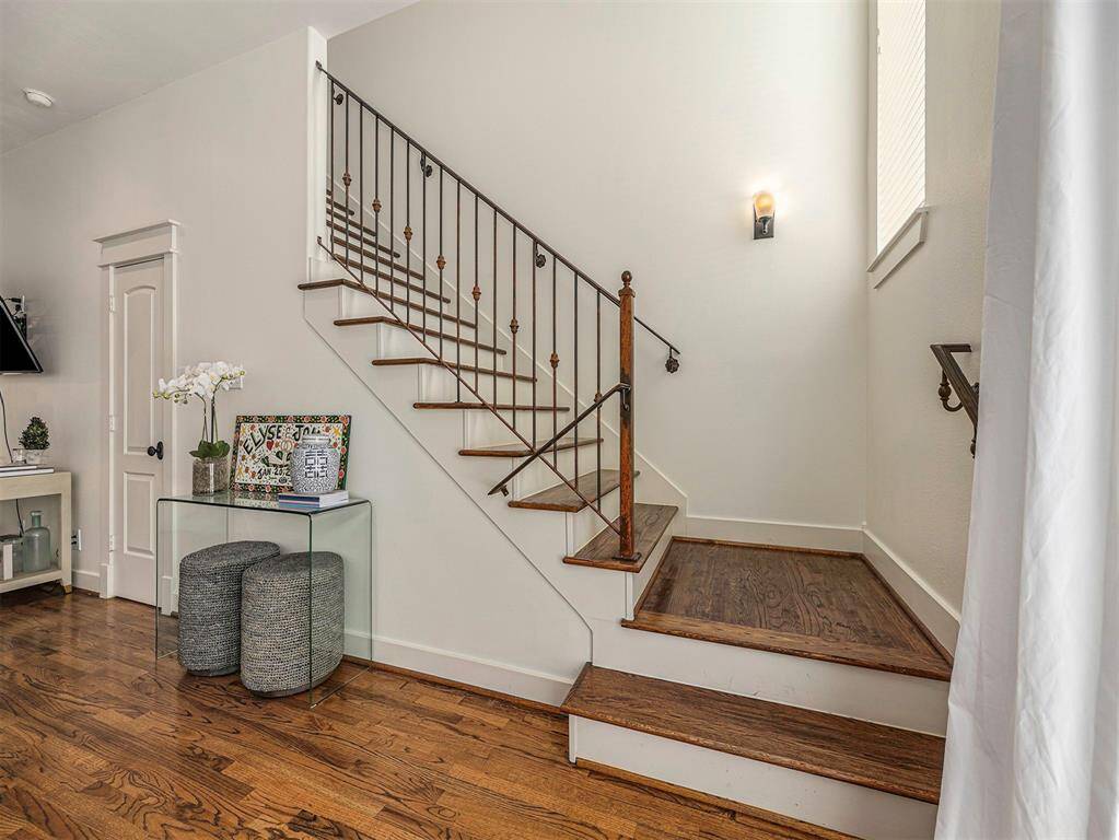 This photo showcases a clean, modern staircase with wooden steps and a decorative metal railing. It features a small, stylish entryway table with decor items, set against a backdrop of light-colored walls and warm hardwood floors, creating a welcoming atmosphere.