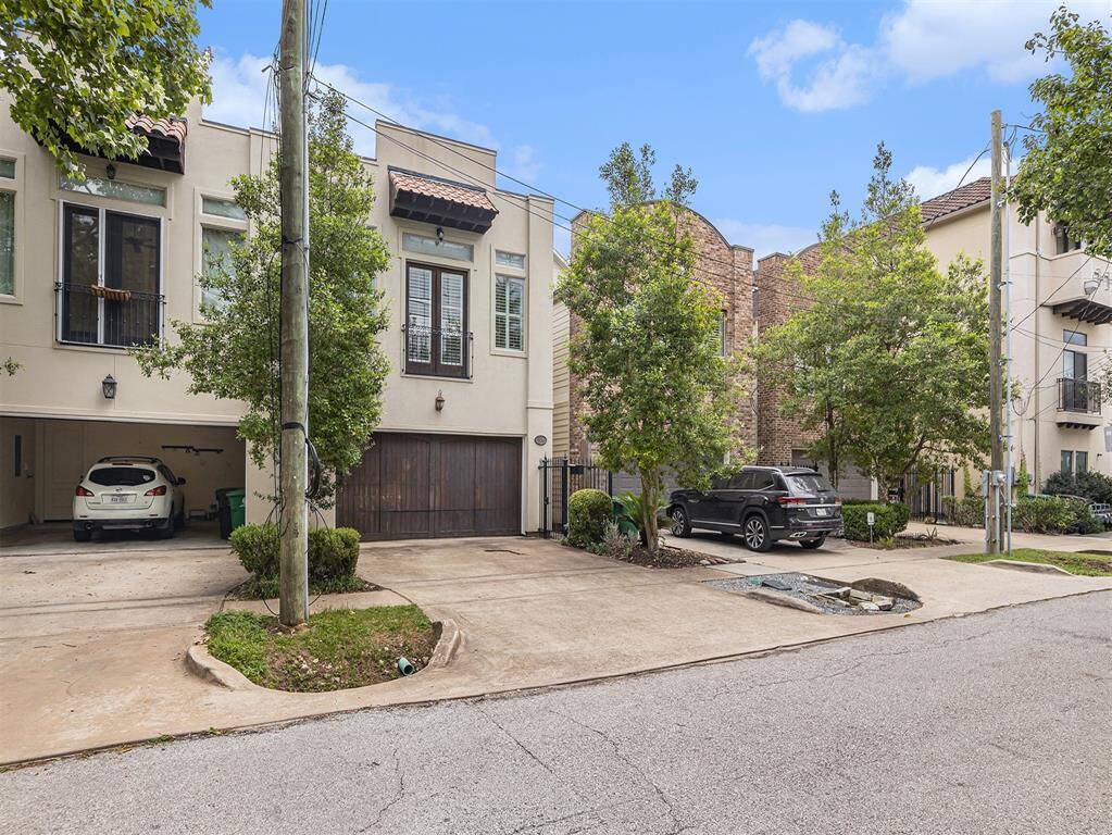 This photo shows a modern townhouse with a stucco exterior and a two-car garage. The home is part of a row of similar houses, featuring a driveway and landscaped front yard with trees. The neighborhood appears quiet and well-maintained.