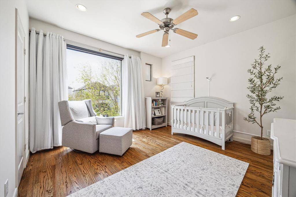 Located upstairs alongside the primary bedroom, this spacious secondary bedroom #1 features a large window overlooking the trees, with pull-down shades and blackout drapes. Two additional windows—one with a roll-down shade and the other with a Roman shade—bring in plenty of natural light. A new wallpaper accent wall adds charm, while the ceiling fan, recessed can lighting, and hardwood floors complete the space. Not shown is an EN SUITE bathroom w/ tub/shower combo & vanity.