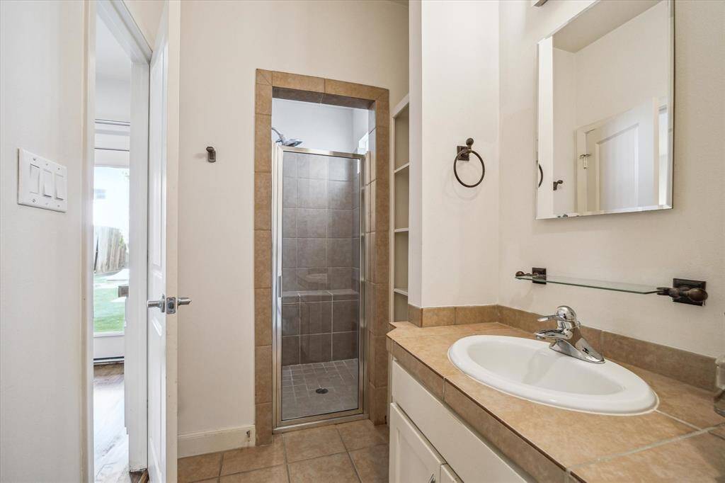 En suite bathroom for secondary bedroom #2 includes a vanity with storage, linen storage, and a walk-in shower with a bench, offering both style and functionality.