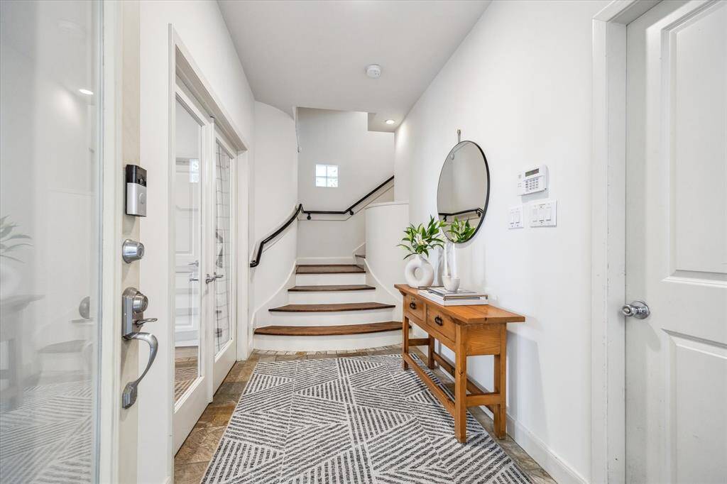 Welcoming entry with space for furniture, a door leading to the attached 2-car garage, tile flooring, and newer sconces illuminating the stairway. French doors open to a downstairs secondary bedroom and the backyard.