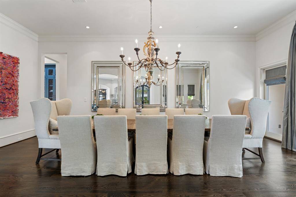This formal dining room offers a refined ambiance with its oversized rustic wood table, plush slipcovered seating, and dramatic antique-style chandelier as the centerpiece. Triple framed mirrors amplify light and space, while rich hardwood flooring and curated art lend warmth and sophistication to the elegant setting.