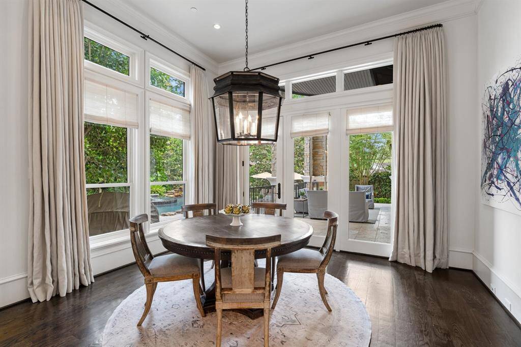 Bathed in natural light and framed by serene garden and pool views, this charming breakfast room offers an inviting setting beneath an oversized lantern-style pendant and elegant floor-to-ceiling drapery.