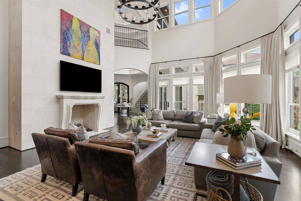 This great room impresses with soaring double-height ceilings, a dramatic limestone fireplace surround, and expansive walls of windows that flood the space with natural light. Thoughtfully layered with plush furnishings, refined textures, and contemporary art, it offers a warm yet sophisticated setting for both relaxation and entertaining.