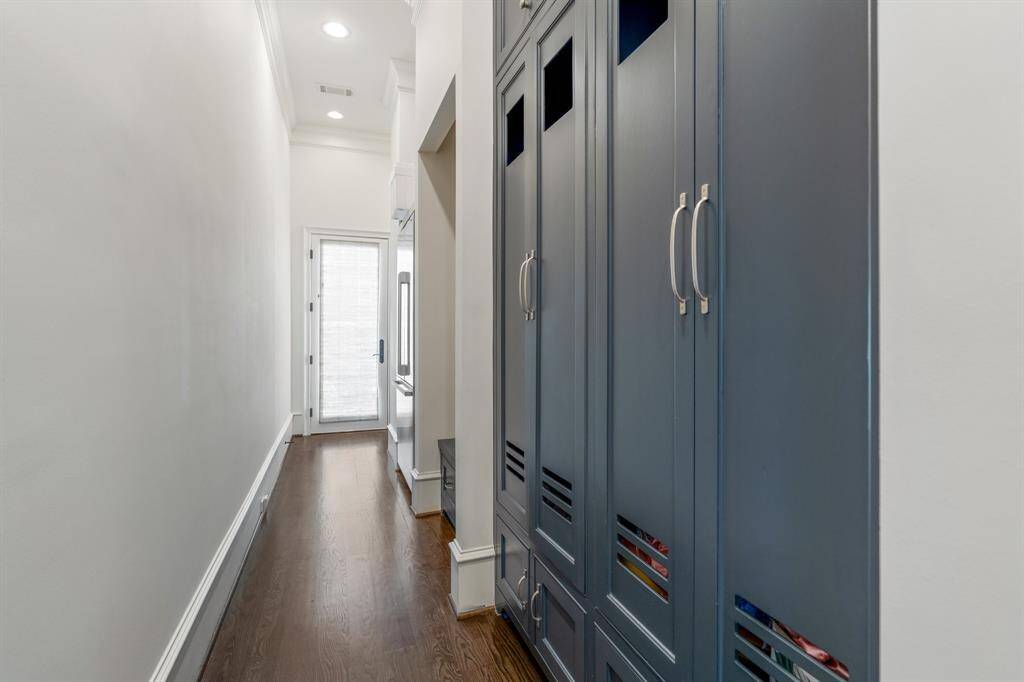 This thoughtfully designed mudroom offers both function and style with custom built-in lockers in a rich slate blue, providing organized storage for everyday essentials. Warm hardwood flooring and natural light from the glass-paneled door create a welcoming transition space between the outdoors and the home's interior.