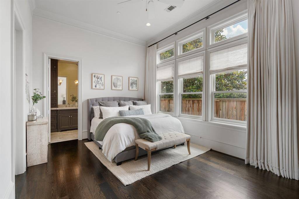 This serene downstairs secondary bedroom offers a restful retreat with its soft neutral palette, oversized windows that flood the space with natural light, and rich hardwood flooring that adds warmth and depth. Thoughtfully appointed with elegant drapery and direct en-suite access, it combines comfort and privacy in a refined setting.