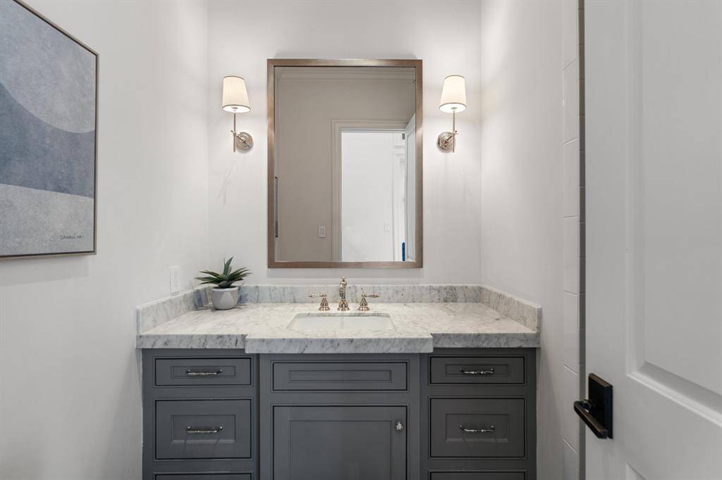 This refined vanity area in the secondary bathroom features a polished marble countertop, elegant gray cabinetry, and warm sconces flanking a sleek framed mirror for a timeless and tailored look.