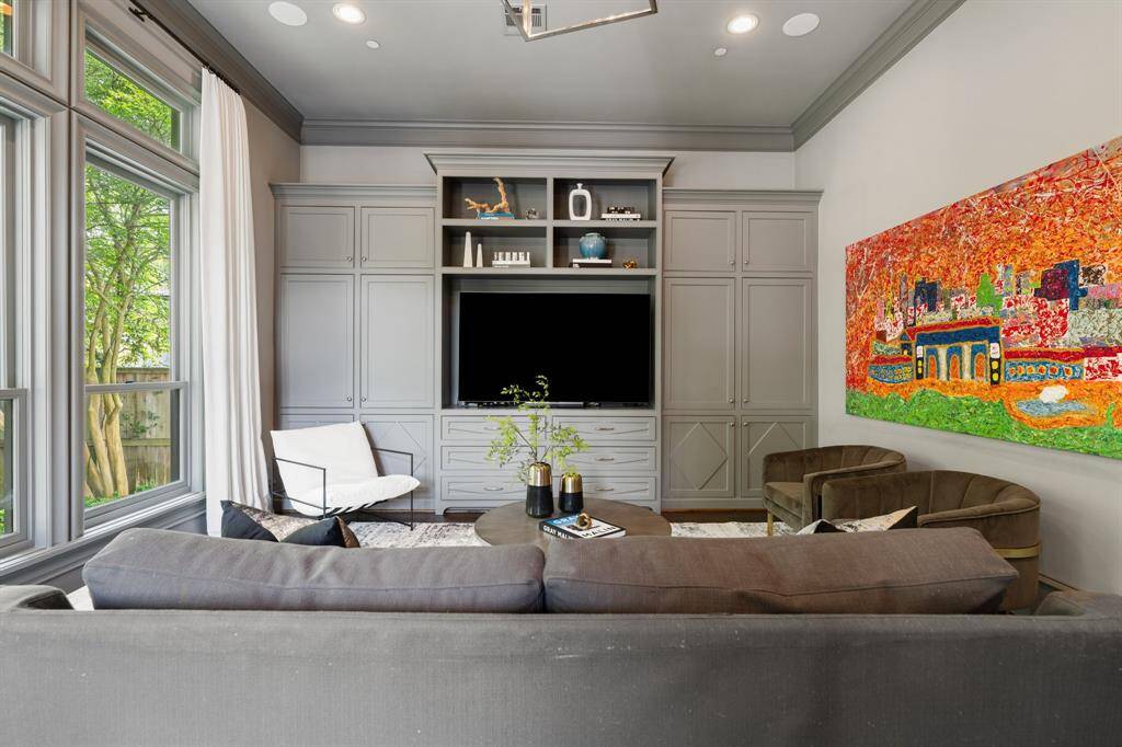 This stylish downstairs game room is anchored by a custom built-in media wall with abundant concealed storage and open shelving for curated display. Bathed in natural light from expansive windows, the space is elevated by bold contemporary artwork, plush seating, and a refined palette perfect for both lounging and entertaining.