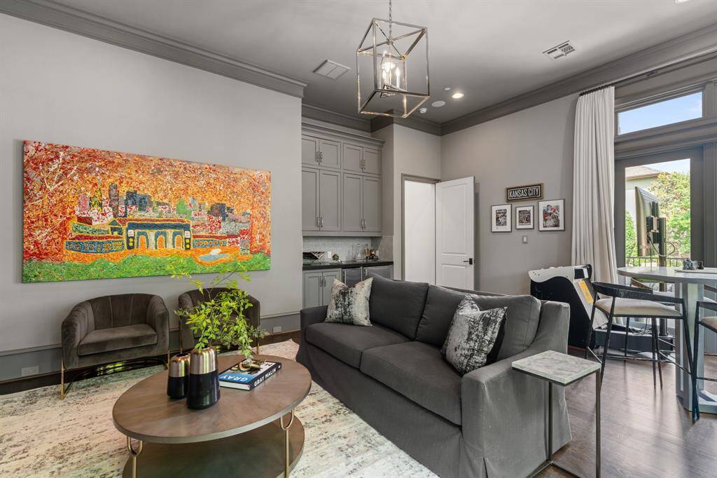This additional view of the downstairs game room reveals a built-in wet bar with sleek cabinetry and a stylish entertainment nook, all framed by dramatic artwork and natural light from expansive patio doors.