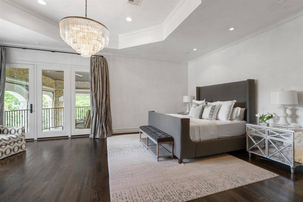 The second-floor primary suite exudes timeless elegance with its soaring tray ceiling, statement crystal chandelier, and rich hardwood floors that anchor the serene ambiance. French doors open to a private terrace, flooding the room with natural light and offering a seamless indoor-outdoor retreat.