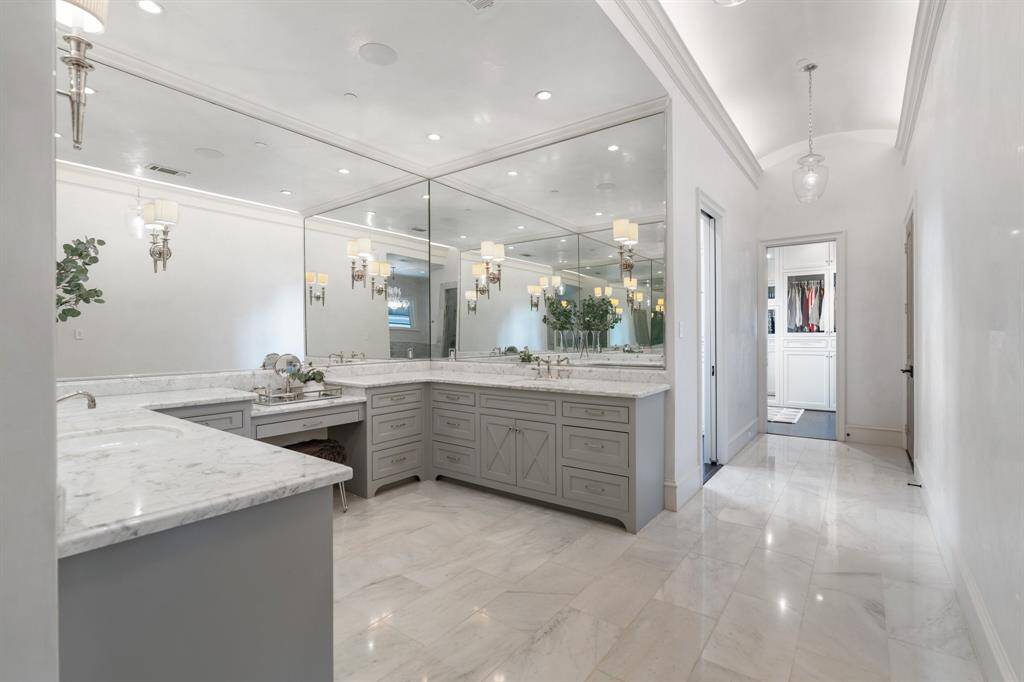 This extended view of the primary bath highlights the luxurious scale and thoughtful layout, seamlessly connecting the dual vanities to an expansive, boutique-style walk-in closet through a graceful arched corridor.