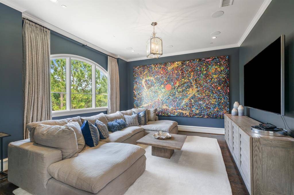 This stylish second-floor media room offers a cozy retreat with rich navy walls, layered textures, and an oversized sectional perfect for movie nights or lounging in comfort. A dramatic arched window brings in natural light, while the vibrant, large-scale art adds a bold visual focal point.