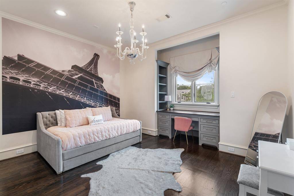 This stylish secondary bedroom evokes Parisian charm with a dramatic Eiffel Tower mural, a tufted daybed, and a whimsical chandelier. A built-in desk nook with open shelving and soft natural light provides a functional and serene workspace.
