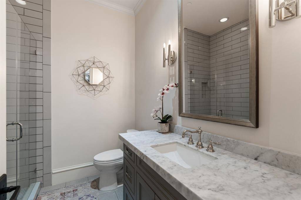 This stylish upstairs secondary bathroom features a sleek marble-topped vanity, polished chrome fixtures, and a frameless glass walk-in shower with contemporary subway tile surround.