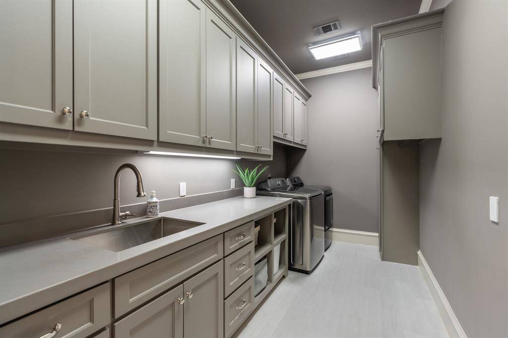 This beautifully designed laundry room features custom cabinetry, sleek quartz countertops, a deep utility sink, and ample storage for a streamlined and functional workspace.