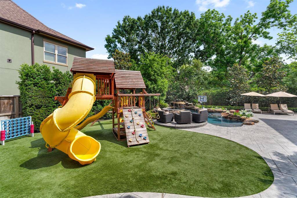 This vibrant backyard features a large turf play area with a custom wooden playground and twist slide, seamlessly blending into the resort-style pool and lounging spaces beyond.