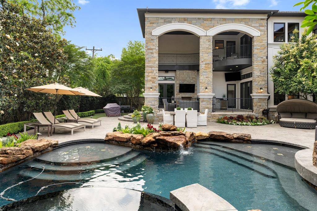 This stunning outdoor retreat showcases a luxurious resort-style pool with rock waterfalls, elevated spa, and lush landscaping that exudes tranquility. The impressive stone-clad covered patio, complete with multiple lounging and dining areas, creates the perfect setting for refined entertaining and relaxed outdoor living.