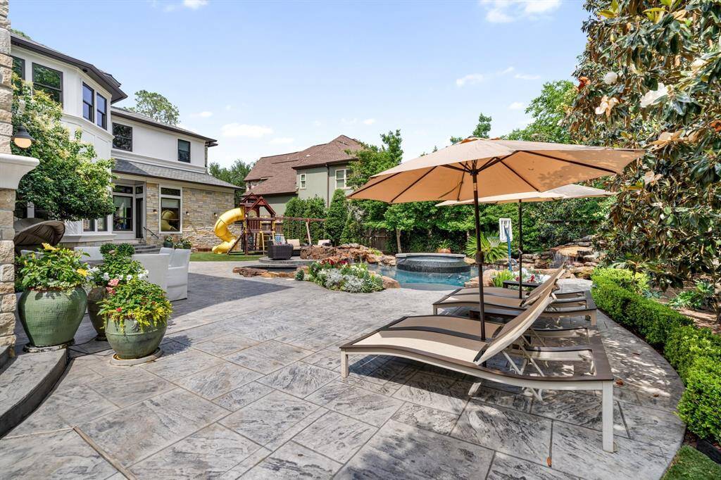 This backyard is designed for both relaxation and recreation, featuring multiple lounge areas, lush landscaping, and a serene rock waterfall cascading into the pool. The space is complete with a sun shelf, spa, and adjacent play area, making it an entertainer's dream and family-friendly haven.