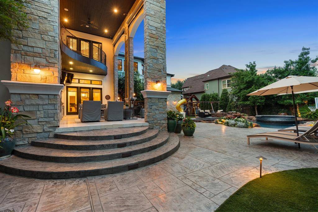 Sweeping stone steps lead to an expansive covered patio that seamlessly blends elegant architecture with inviting outdoor comfort. The lushly landscaped backyard showcases a sparkling pool, waterfall spa, play area, and sun-soaked lounging zones, creating a private resort experience at home.