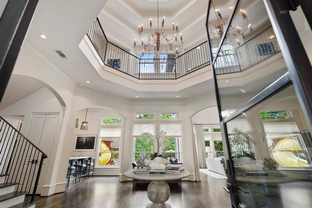 This grand two-story foyer makes a striking first impression with its soaring tray ceiling, elegant wrought-iron staircase, and dramatic chandelier that draws the eye upward. Natural light pours through expansive windows, illuminating the exquisite architectural details and refined symmetry of this sophisticated entryway.