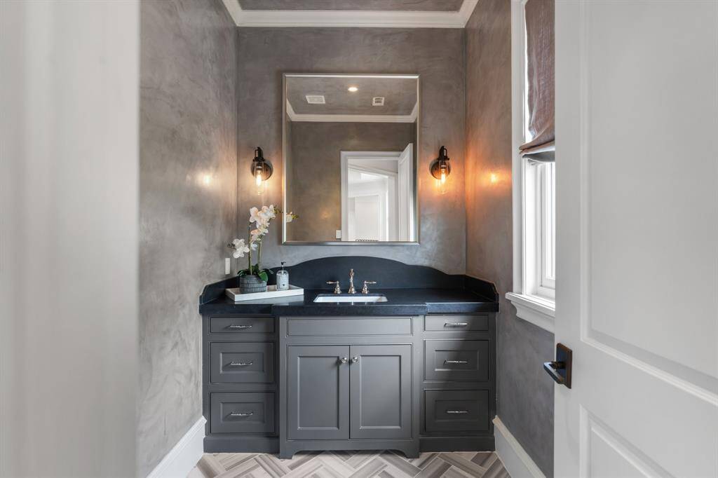 This sophisticated powder room features a moody, polished plaster finish, custom charcoal vanity with sleek hardware, and contemporary lighting that adds a warm, ambient glow.