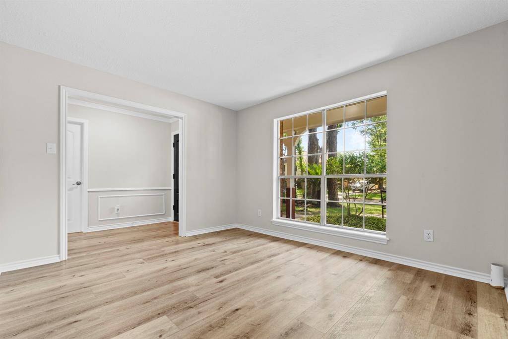 Another view of the formal living room that has neutral paint, white accents, LVP flooring, and great windows lookng out to the front of the house.