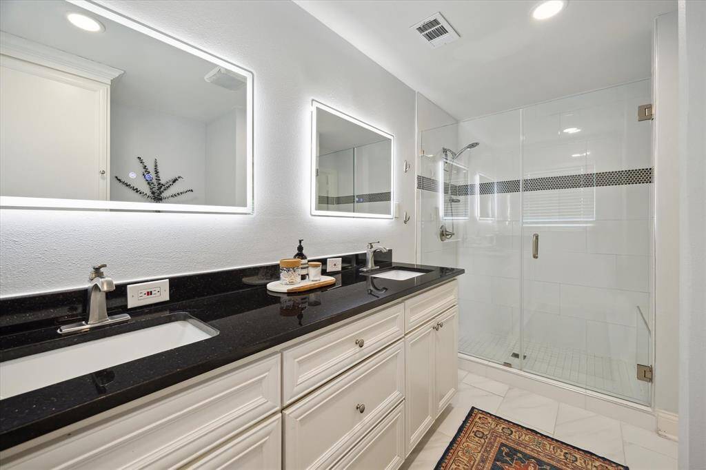 The updated primary bath with double sinks, double lit mirrors and thelarge frameless glass and tile shower.