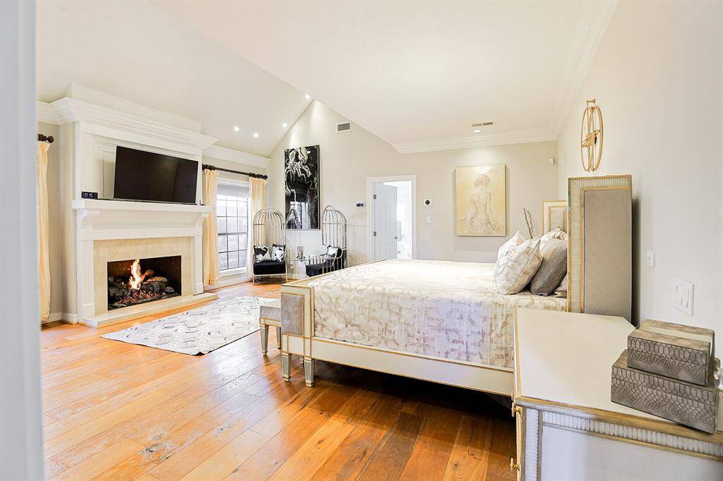 A luxurious and spacious primary suite featuring vaulted ceilings, a cozy fireplace, and a serene seating area. Crystal chandeliers and elegant decor elevate the room’s sophistication, while large windows bring in natural light, creating a warm and inviting retreat.