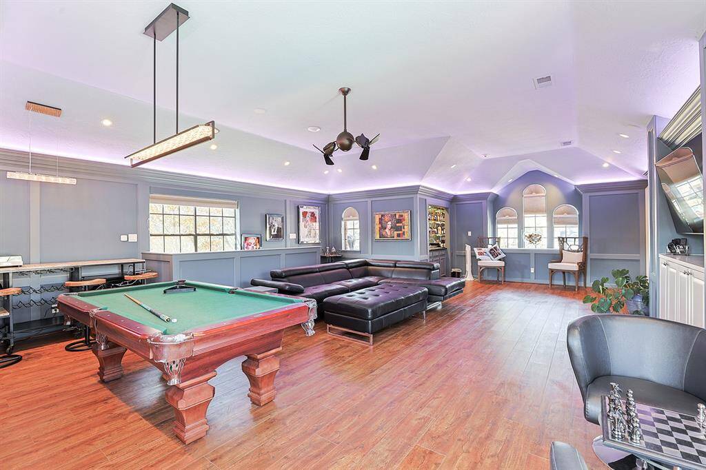 A sophisticated and spacious game room with a vaulted ceiling, wood flooring, and LED accent lighting. This space is perfect for entertaining, featuring a pool table, built-in bar, and comfortable seating.